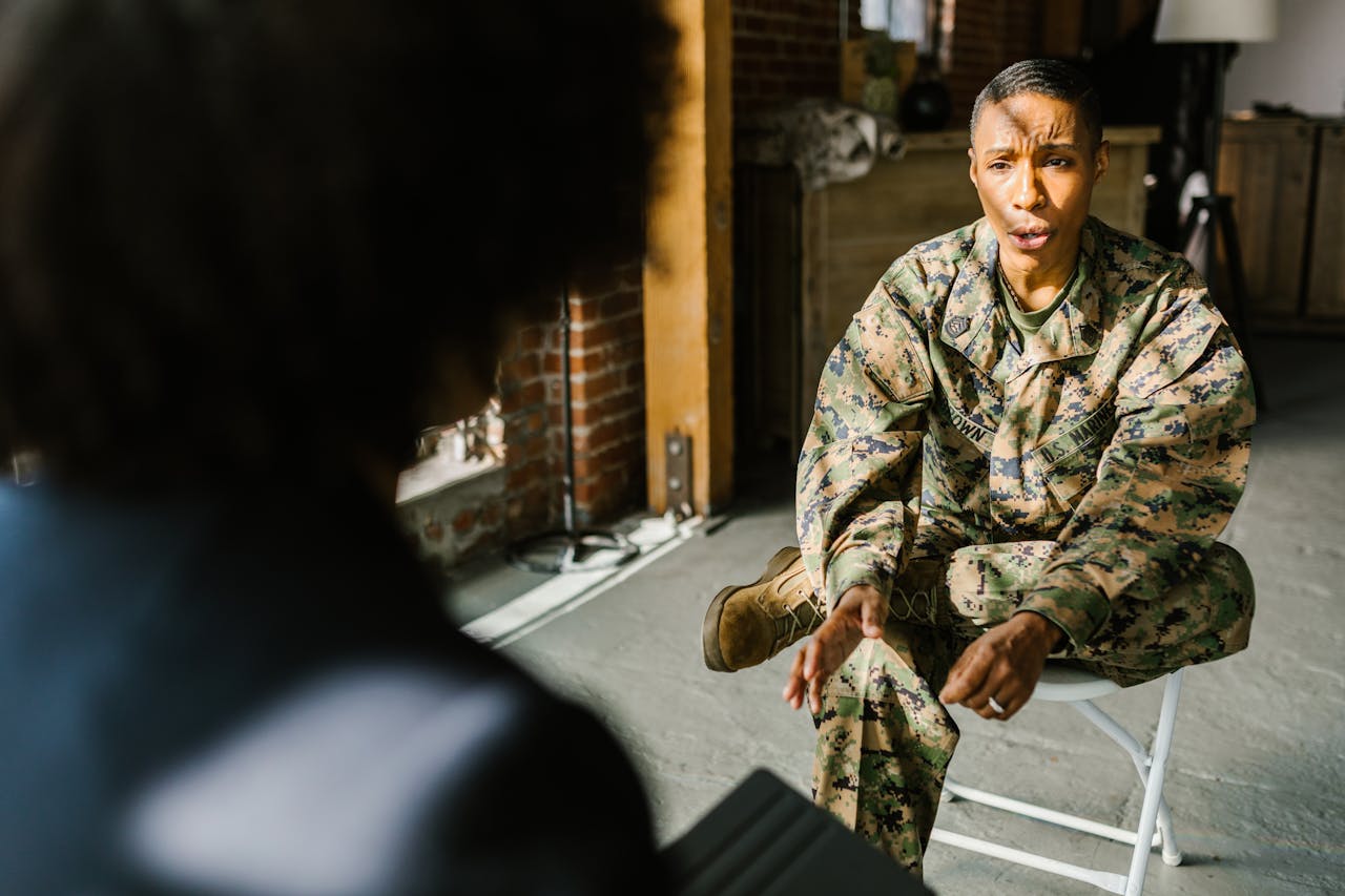 A soldier in military uniform during a therapy session indoors, discussing with a counselor.